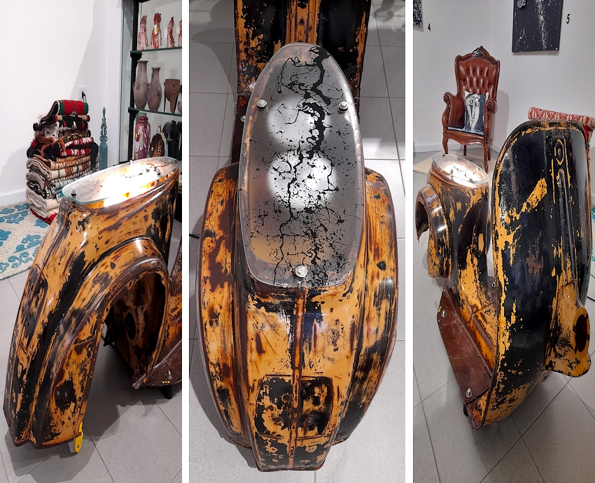 Vista notturna con la scultura illuminata. Questa scultura è stata realizzata col telaio di una Vespa d'epoca 50 special. La sua patina color ruggine le dona una linea elegante ed al tempo stesso contemporanea e moderna. Grazie ad un impianto elettrico, la scultura diventa una lampada da pavimento che trasmette un ampio fascio di luce verso l'alto grazie a due lampade led inserite nel vano sotto sella. Scultura moderna dedicata a tutti coloro che amano l'old stile ed il vintage; scultura che donerà un tocco unico all'arredamento di una casa moderna.