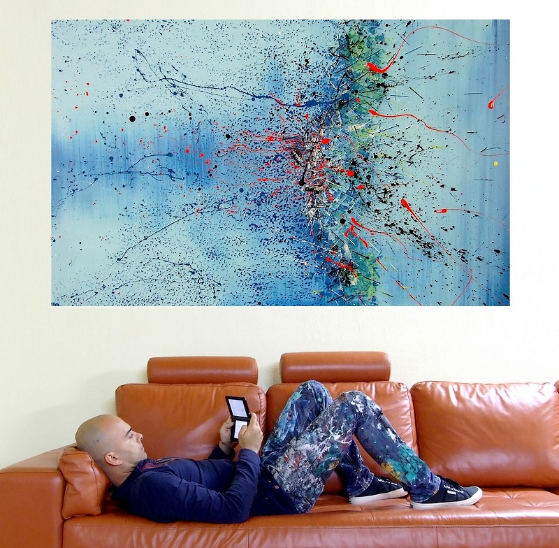 L'artista e pittore contemporaneo Goa in posa con i suoi più bei quadri astratti moderni fatti a mano. In questa fotografia sopra un divano moderno color marrone chiaro la tela dal titolo: ho scritto ti amo ma non ricordo dove